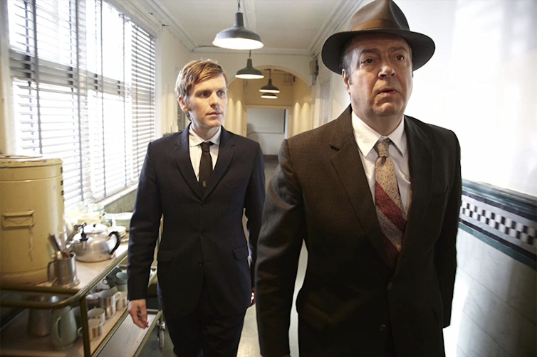 Younger man walks behind older man in hallway, looking to him for guidance.