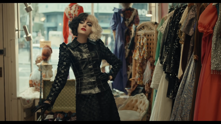 Emma Stone dressed as Cruella de Vil wearing black and white wig and black leather outfit in a shop