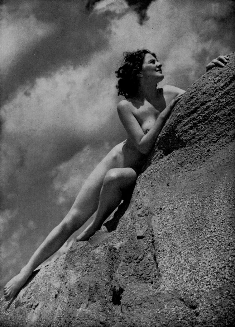 A slim nude woman reclines on a rock against the sky