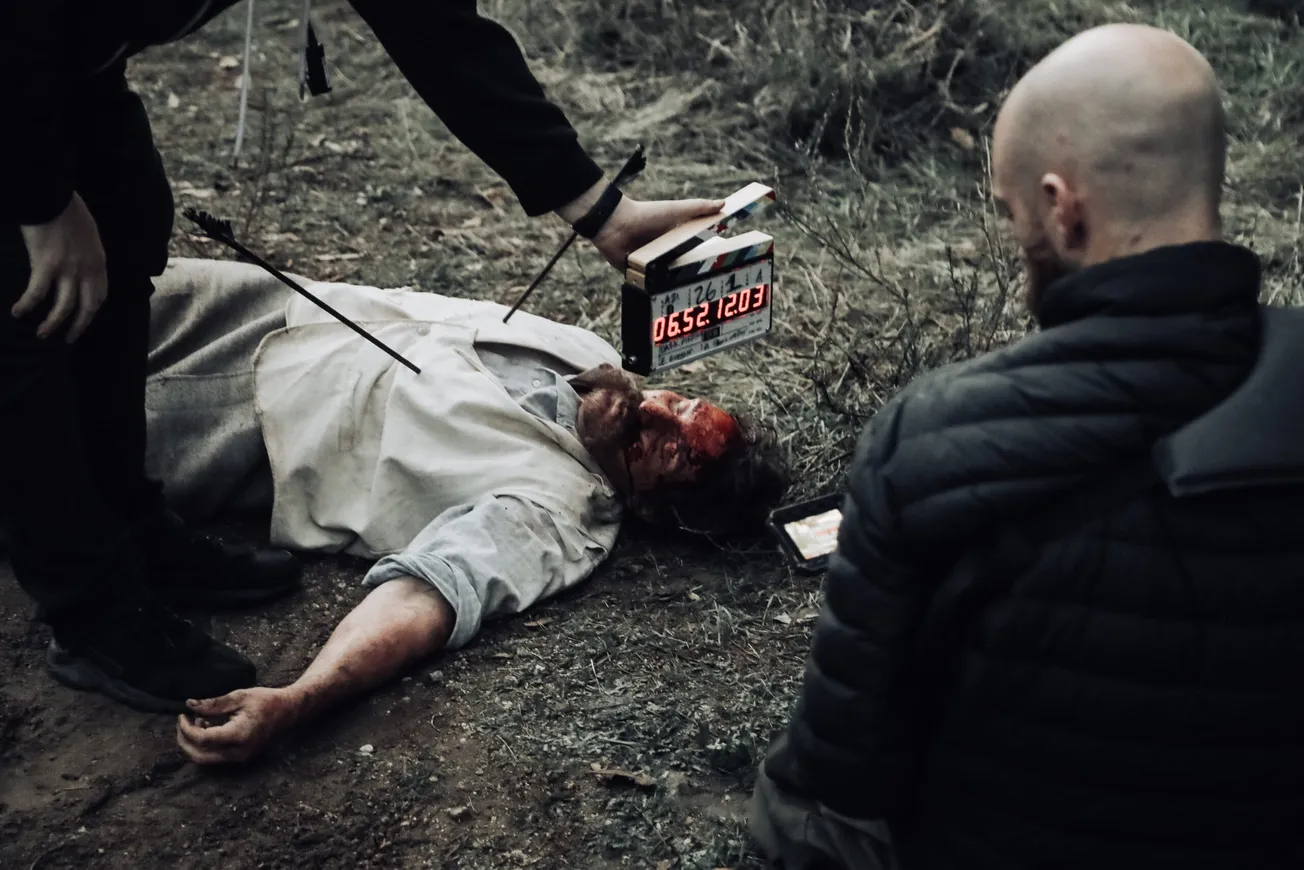 man in black bubble jacket facing man in white shirt lying on the ground while man in black bottoms holding digital time devi