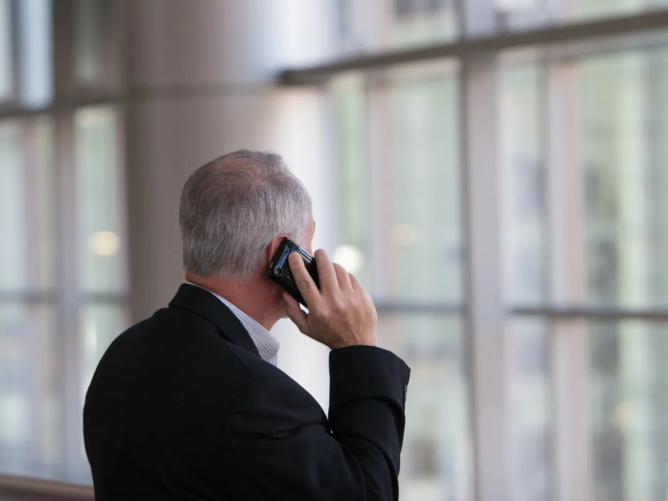 man holding black smartphone in front of a windowpane