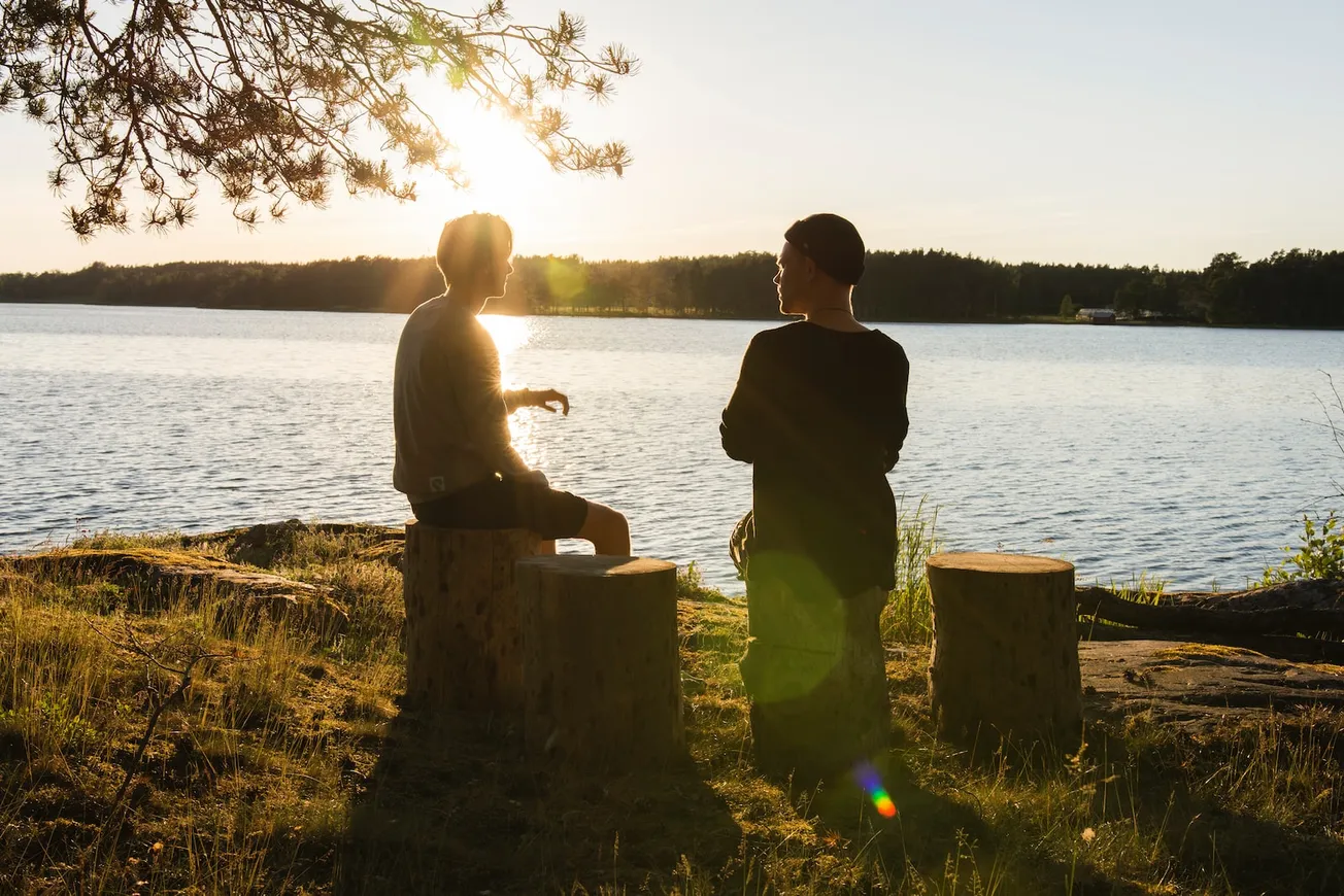 man in black jacket standing beside body of water during sunset