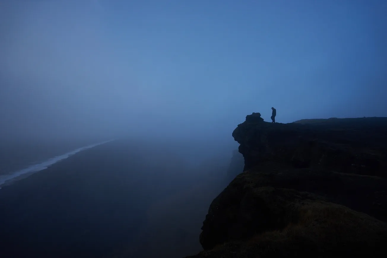 person standing rock cliff covered with fog