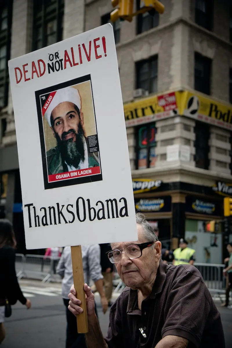 man sitting holding Dead Not Alive! Thanks Obama placard