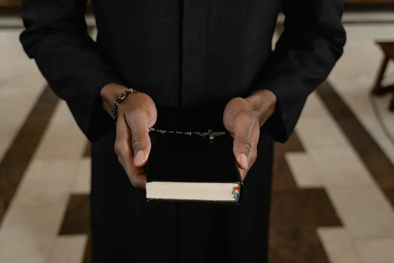 A Close-Up Shot of a Priest Holding a Bible and a Rosary